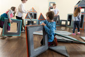 Two preschool-aged children working together to build a tall magnetic tile structure in a classroom setting, demonstrating hands-on STEM learning through large-scale, open-ended play.