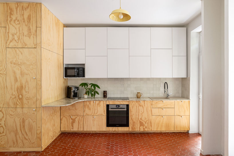 Cuisine ouverte sur salon avec façades en contreplaqué de pin et sol en tommettes – rénovation d’une maison individuelle à Marseille par Violaine Planchard Architecture.