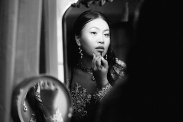 black and white photojournalistic style image of bride applying make up in film noir lighting