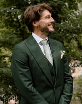 Groom wearing a green tux watching his bride walk down the aisle during their wedding ceremony in the white mountains