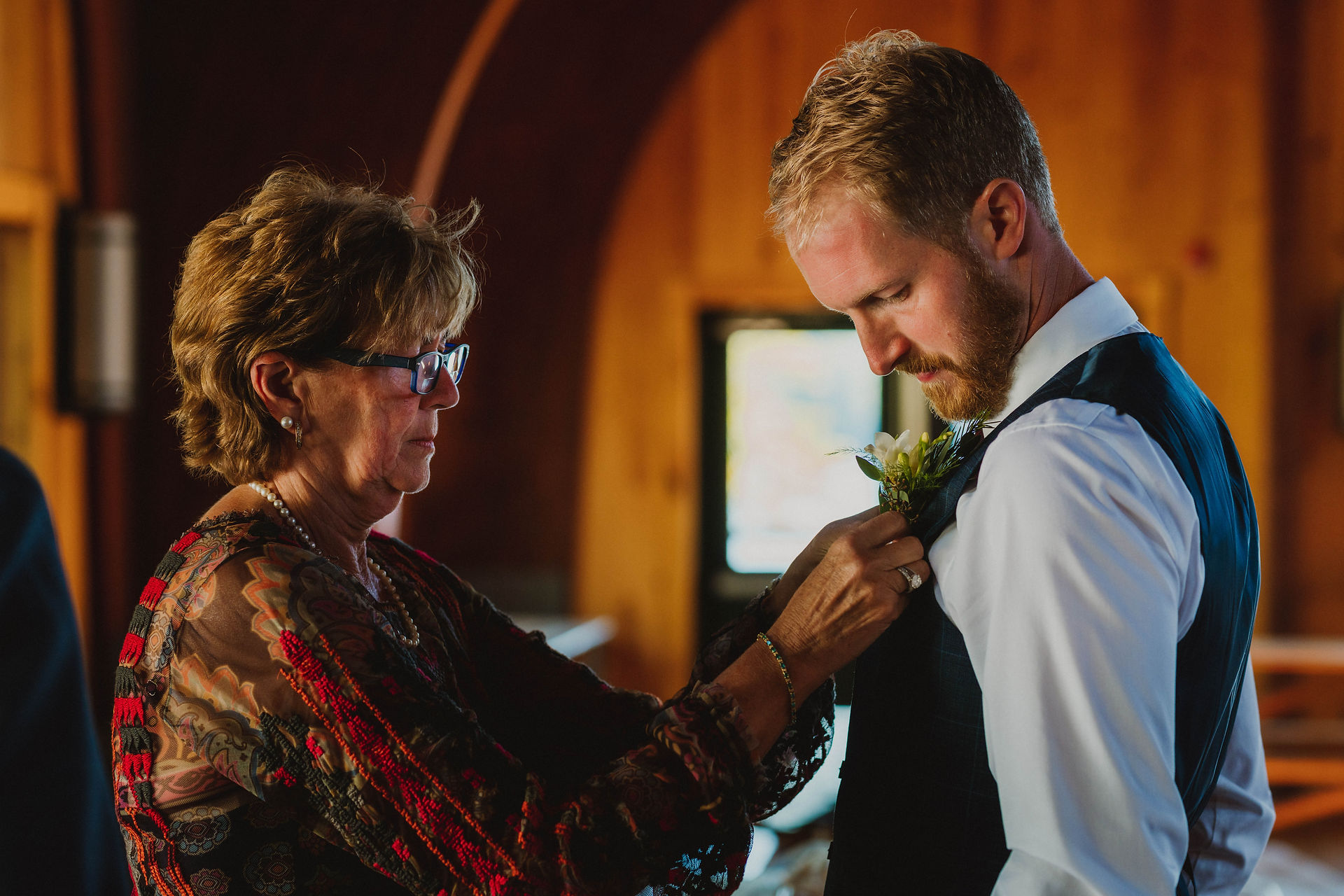 groom having his boutonniere pinned on by mother of the bride 
