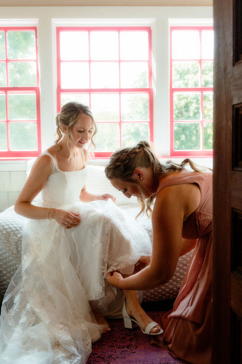 A bridesmaid helping a bride put her wedding shoes on in Maine