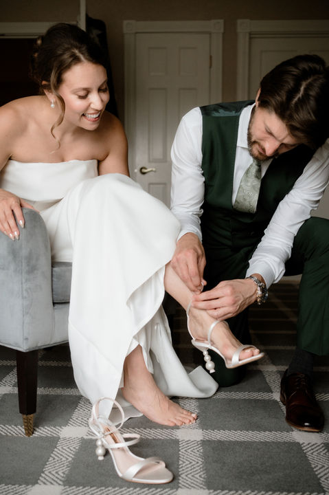 Bride getting dressed with the groom as he puts her shoes on for her at the Wentworth Inn in New Hampshire
