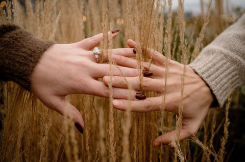 Close up of a man and woman's hands interlocked amongst tall grasses during an engagement session at Piers Park in Boston. 