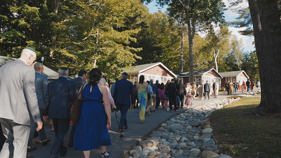 Wedding guests walk a tree-lined stone path toward the reception cabins at Camp Manitou in Oakland, Maine