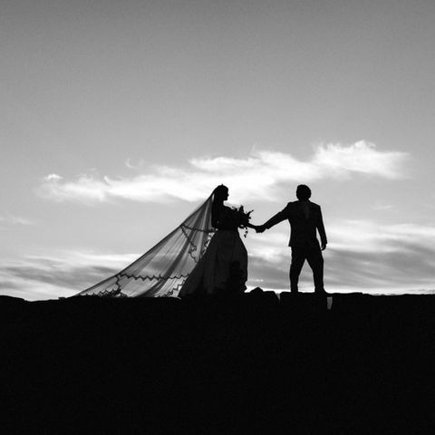 Bride and Groom black and white silhouette with groom leading bride while walking and bride's veil is extended behind her during sunset portraits at The Colony Hotel in Kennebunkport, Maine