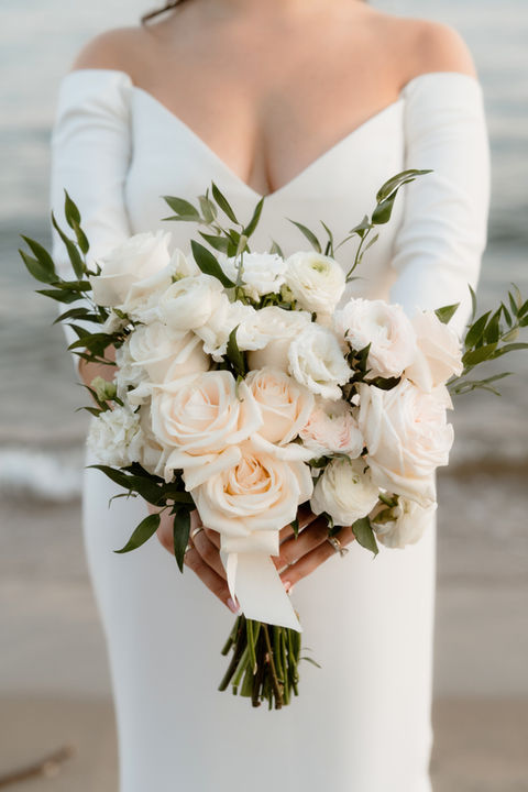Close up of a bride's white bouquet being held out on a beach in Rhode Island during a wedding.