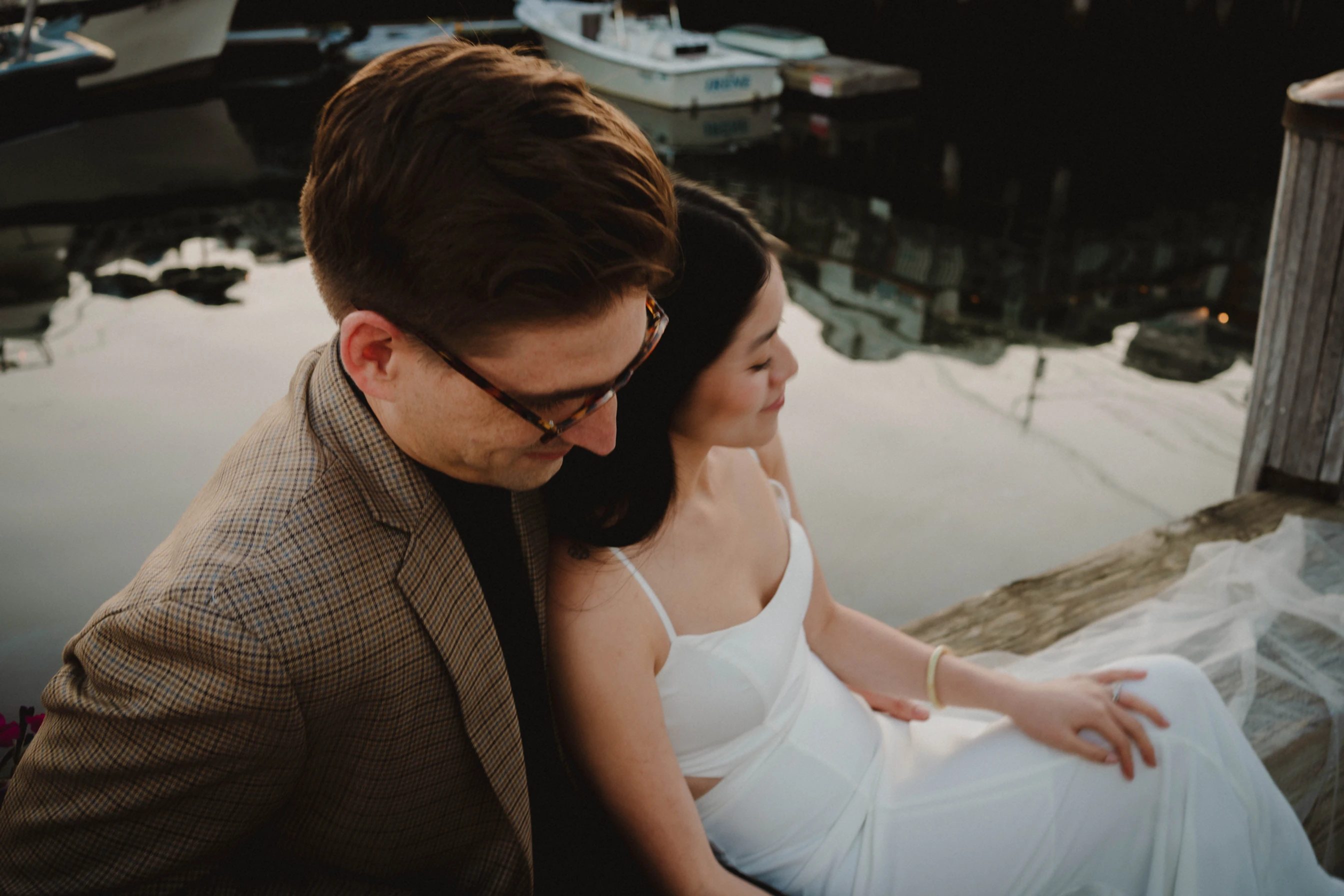 bride and groom cuddling while sitting on a dock during a Portland, Maine elopement