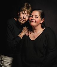 A professional portrait of a mother and daughter leaning against each other with a black backdrop