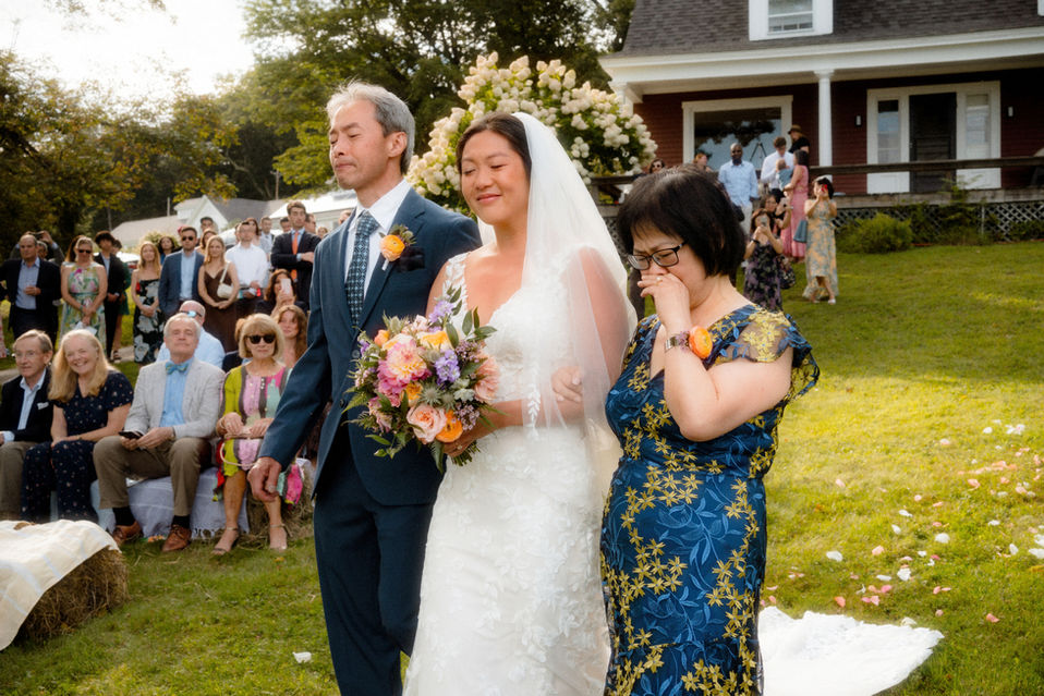 A bride and her parents crying as they walk down a wedding aisle in New Hampshire.