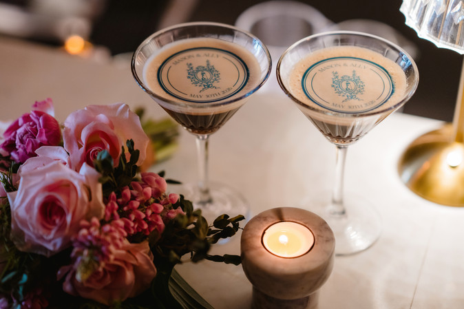 Overhead view of two custom Mason and Ally espresso martinis next to a votive candle and pink rose bouquet at Apero
