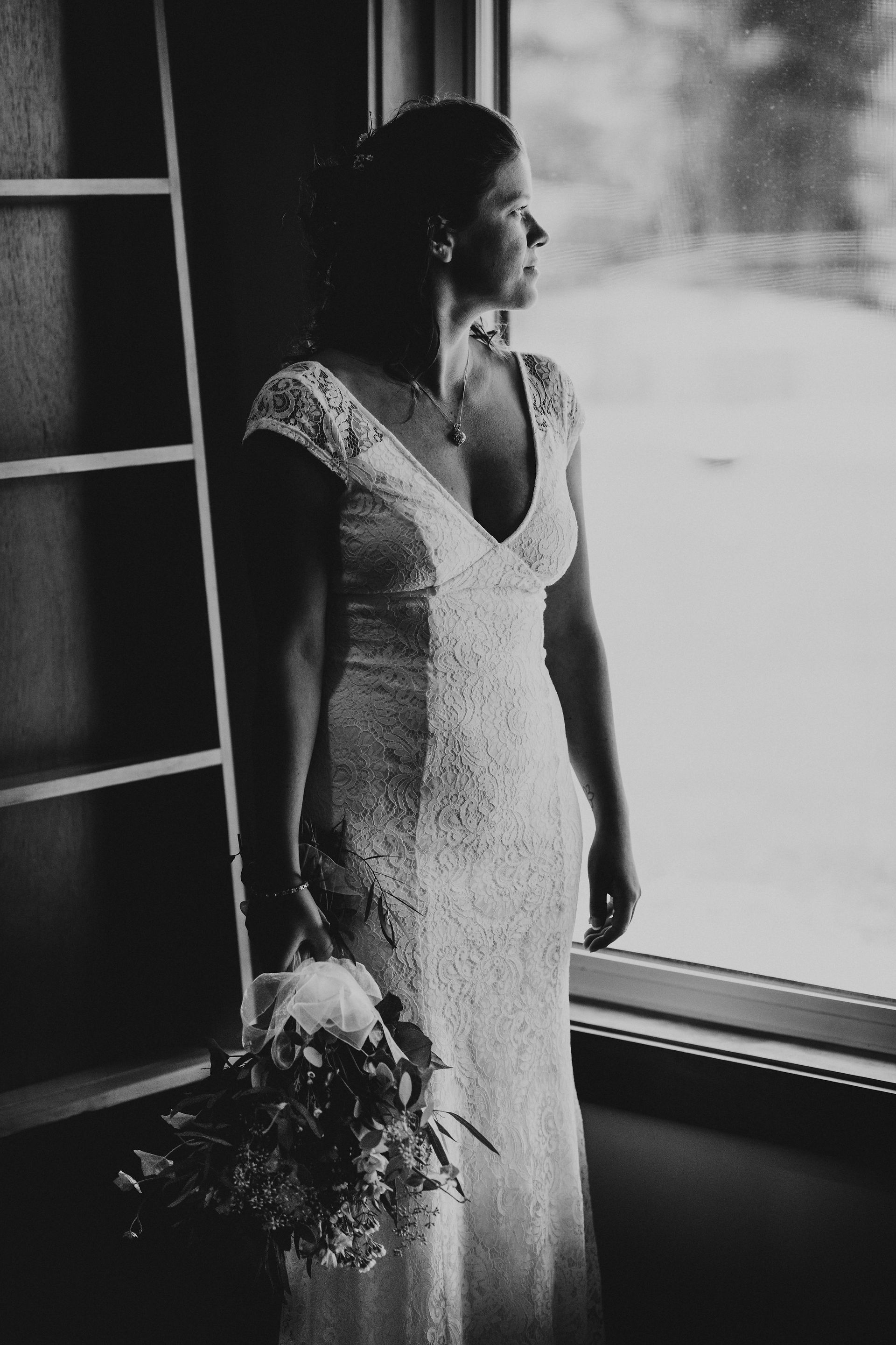 black and white image of bride holding her bouquet by a window