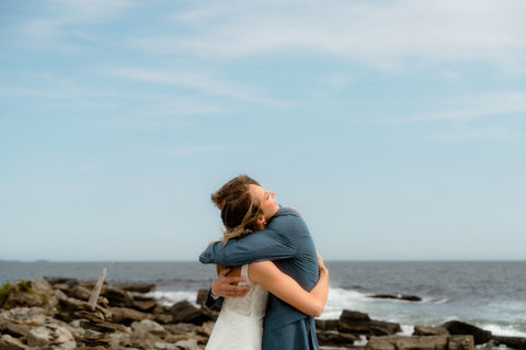 A bride and groom hugging tightly on a rocky coastline in Maine.