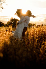 A woman being held up in a man's arms and leaning her head back during sunset in a wheat field during an engagement session in Biddeford, Maine