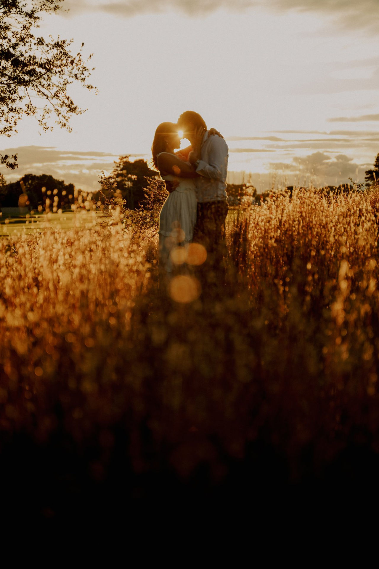 A woman and man standing in a field of tall grasses during glowing golden hour light.