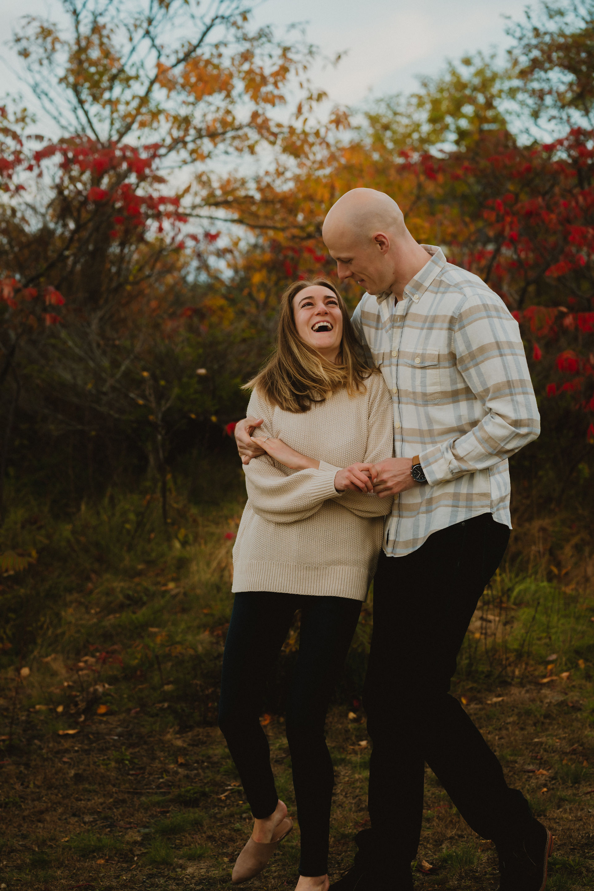 couple laughing with new england fall foliage behind them 