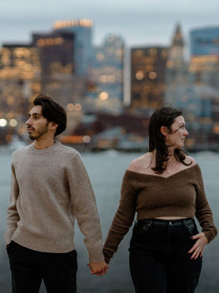 Man and woman holding hands with the Boston skyline behind them in the Fall.