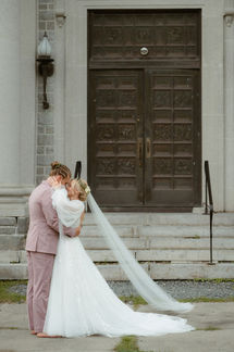 A bride and groom embracing outside of a large stone building in New Hampshire.
