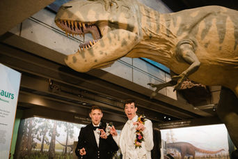 Two gay grooms being funny during their wedding portrait session under the T-rex at the Boston Museum of Science