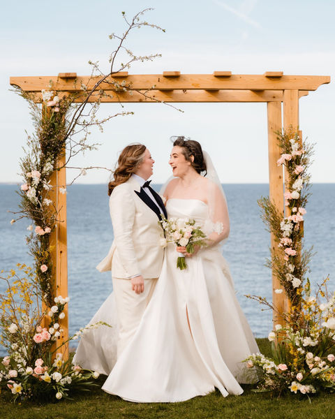 two lesbian brides embracing under their wedding arch at The Cliff House Maine in Cape Neddick