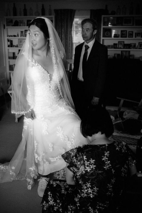 Black and white image of a bride getting help putting on her shoes in New Hampshire.