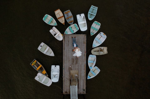 Drone photo of bride and groom laying down on a dock surrounded by small sailboats during sunset at TEIA club on Peaks Island in Maine