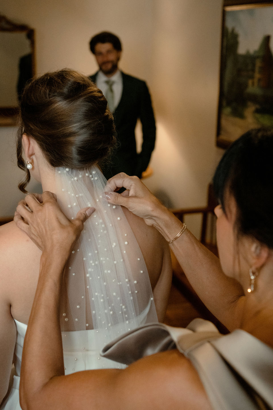 Bride's mother putting veil into her hair as the groom looks on at The Wentworth Inn, NH.