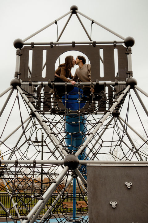 A man and woman kissing inside of a tall jungle gym during an engagement session at Piers Park in Boston.