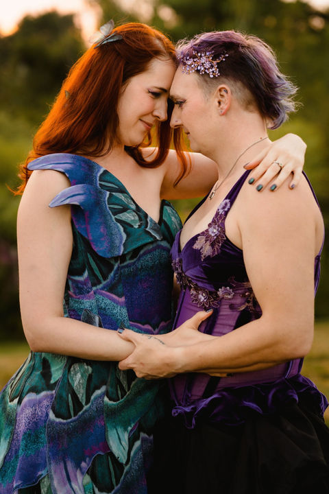 A queer couple in colorful wedding dresses embracing during sunset photos at Flaherty's Family Farm in Scarborough, Maine