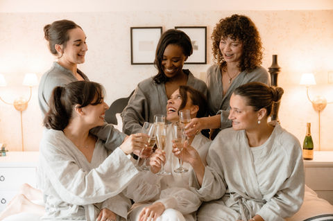 Bride and bridesmaids sitting on a bed with champagne and laughing at The Wentworth Inn, NH 