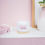 Thumbnail: Geranium and Eucalyptus candle open sitting on its lid, on a shelf with pink background