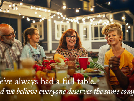 Happy multigenerational family laughs around a food-laden outdoor dinner table under string lights; text reads about a full table.
