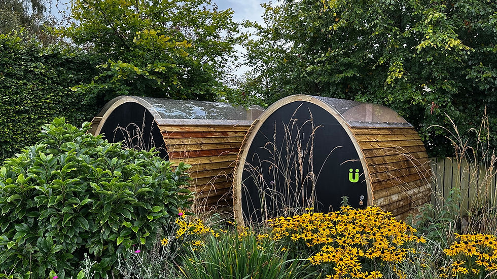 Two curved sheds with transparent roofs set in a beautiful garden.