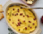 A dish of golden dip dotted with dark red pomegranate arils, and a sprig of oregano, pita chips, a tray of crackers and a small dish of pomegranate arils are also on the counter.