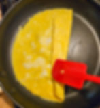A pan with egg in it; there is a red silicone spatula folding the egg over on top of itself