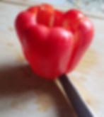 A knife slicing down one side of a red bell pepper.