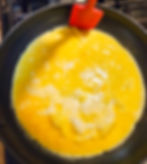 A skillet filled with egg; there is a red silicone spatula pushing egg down around the edges