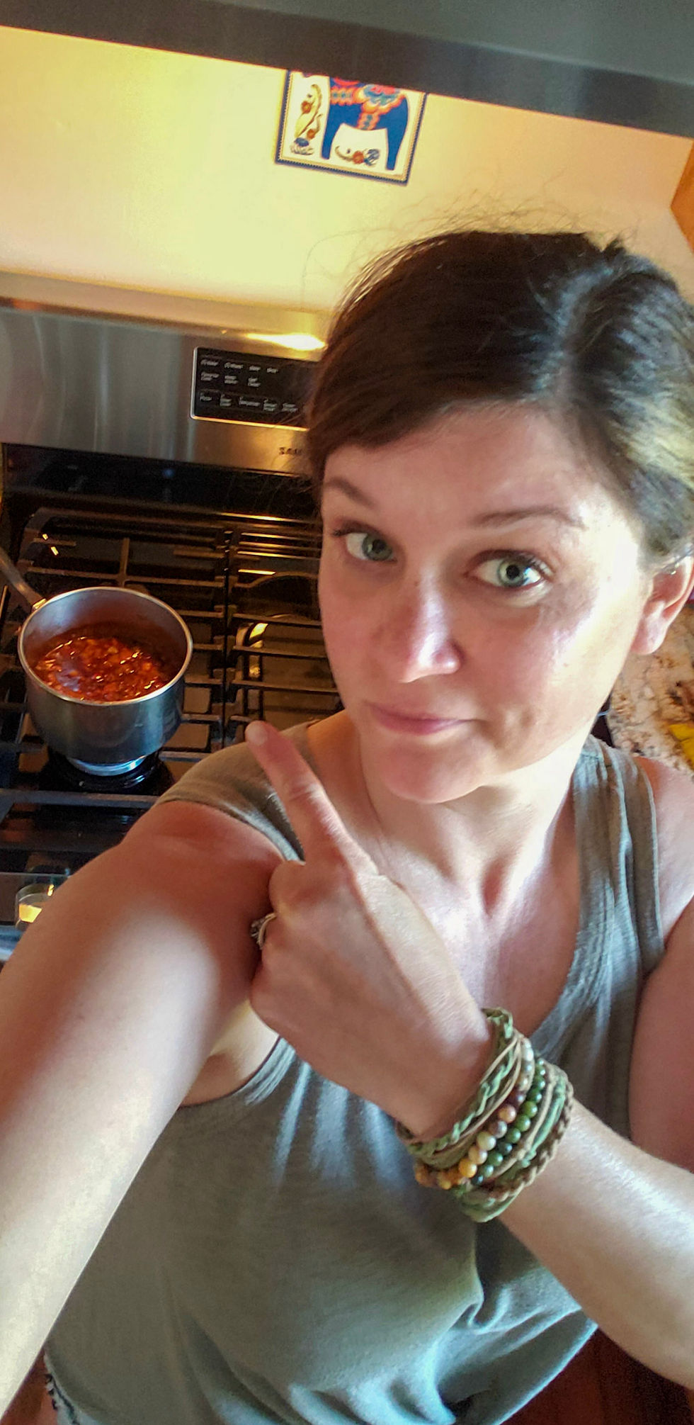 The website author taking a selfie, pointing over her shoulder to a pan simmering on the stove.