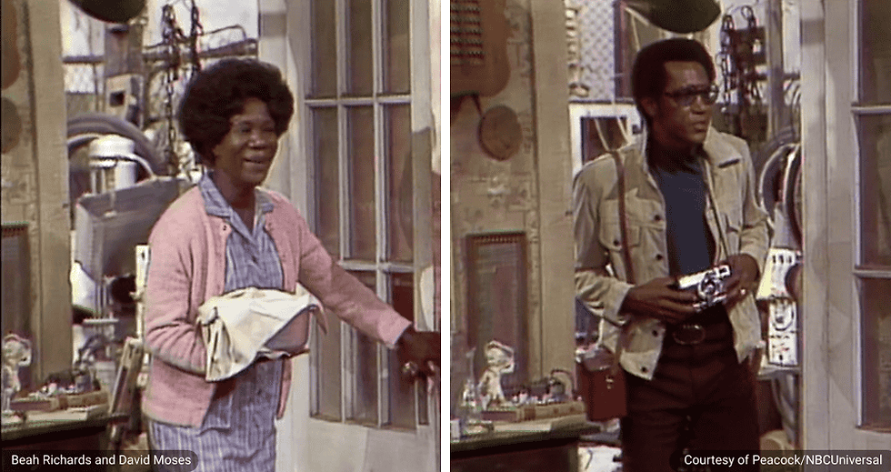 Aunt Ethel, played by Beah Richards, stands inside the Sanford & Son living room. She wears a light pink cardigan and holds a folded cloth or garment. Beside her, a robber, played by David Moses, wears a tan jacket, dark shirt, glasses, and holds a small camera or handheld device. Shelves and household items are visible behind them.
