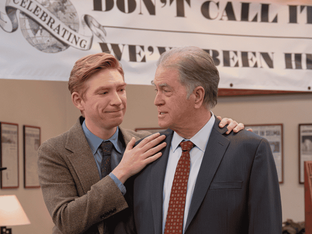 Ned (Domhnall Gleeson) puts his hand on Marv Putnam’s (Allan Havey) shoulder in the newsroom office with a 125th anniversary banner in the background.