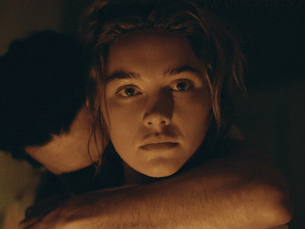 Christopher Abbott as Adam Trask embraces Florence Pugh as Cathy Ames, who looks ahead in a dimly lit room.