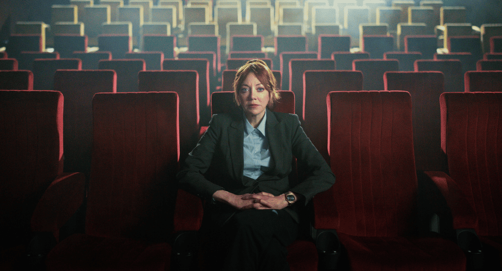 Cunk on Cinema: Diane Morgan as Philomena Cunk sits among rows of red cinema seats.