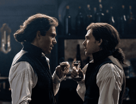 Actors François Civil and Kit Harington as Sydney Carton and Charles Darnay, facing each other with wine glasses in a dark period room.