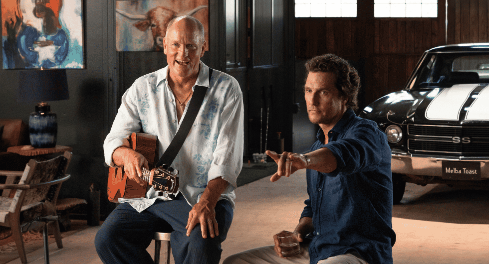 Woody Harrelson holding a guitar and Matthew McConaughey sit in a room with a black vintage car behind them for the show Brothers.