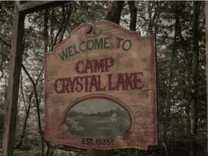A wooden Camp Crystal Lake entrance sign hangs among trees in the Peacock series starring Linda Cardellini as Pamela Voorhees.