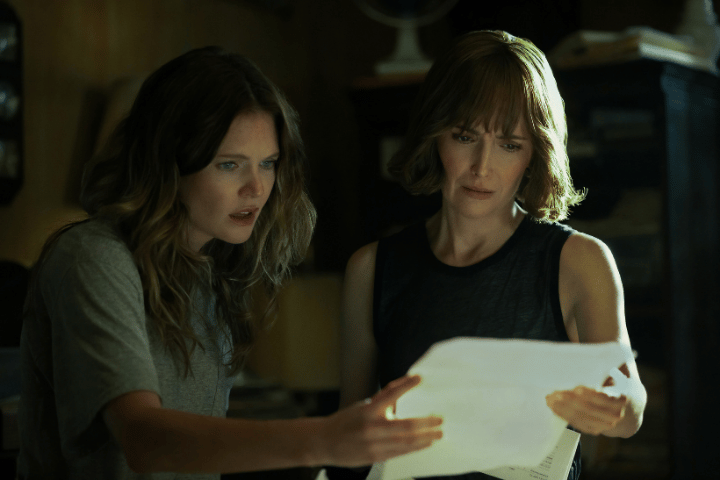 The Good Daughter, Meghann Fahy and Rose Byrne examine documents together inside a dimly lit room.