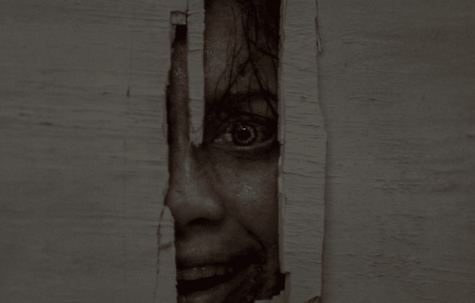 Evil Dead Burn shows a person's face and one eye through a narrow opening in a wall.