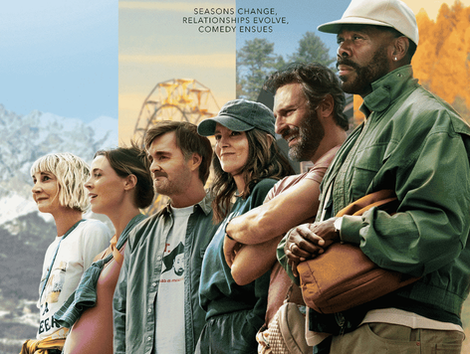 The cast of The Four Seasons, including Tina Fey and Colman Domingo, stands outdoors in casual layers against a soft, colorful autumn backdrop.