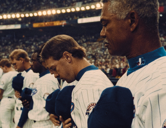 Montreal Expos players stand side by side with caps held to their chests, heads lowered.