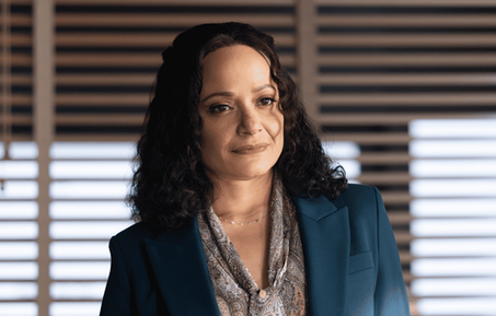 Judy Reyes as Lt. Selena Soto stands in an office wearing a teal blazer and patterned blouse in the High Potential episode Family Tree.